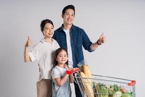 Bild von asiatisch Familie schieben ein Supermarkt Wagen während Einkaufen, isoliert auf Weiß Hintergrund foto