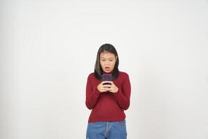 jung asiatisch Frau im rot T-Shirt Beeindruckend schockiert während mit Smartphone isoliert auf Weiß Hintergrund foto