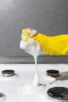 Hausfrau im Handschuh schrubben das Oberfläche von Gas Herd mit Schwamm und chemisch Schaum. Vertikale Foto. Zuhause Reinigung Konzept, Küche Hygiene foto