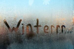 Winter gefroren Fenster. kreativ Rechtschreibung von das Wort Winter, meint kalt und Einfrieren. eisig Muster auf Glas, sonnig Morgen. foto