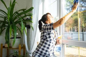 Frau manuell wäscht das Fenster von das Haus mit ein Lappen mit sprühen Reiniger und Mopp Innerhalb das Innere mit Weiß Vorhänge. Wiederherstellen bestellen und Sauberkeit im das Frühling, Reinigung warten foto