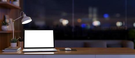 ein modern Büro auf ein Wolkenkratzer beim Nacht mit ein weißer Bildschirm Laptop Computer auf ein hölzern Tisch. foto