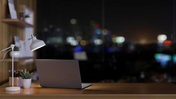 ein Laptop Computer, ein Tabelle Lampe, und Dekor auf ein Schreibtisch in der Nähe von das Fenster mit ein Nachtzeit Sicht. foto