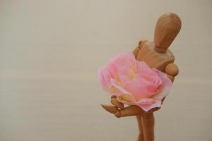 hölzern Mannequin halten ein Rosa Rose auf ein hölzern Hintergrund foto
