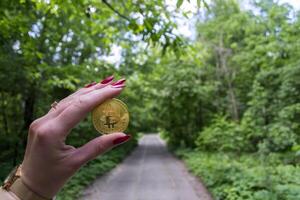 golden Bitcoin im Frau Hand gegen ein Grün Pfad Hintergrund. foto