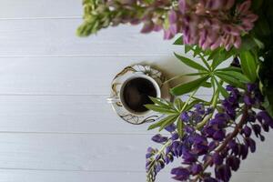 ein Tasse von Kaffee und Lupine Blumen auf ein Weiß hölzern Tisch. foto