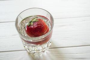 reif Erdbeere im ein Glas mit Wasser auf ein Weiß hölzern Tisch. foto
