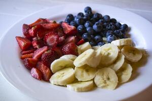 Teller mit Bananen, Erdbeeren und Blaubeeren. foto