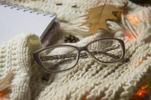 Brille, Notizblock und Herbst Blatt auf das gestrickt Plaid. Winter eben legen. Hygge Stil. foto