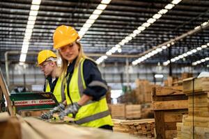 Frau Reinigung Bauholz Holz im dunkel Warenhaus Industrie. Mannschaft Arbeiter Zimmermann tragen Sicherheit Uniform und schwer Hut Arbeiten und Überprüfung das Qualität von hölzern Produkte beim Werkstatt Herstellung. foto