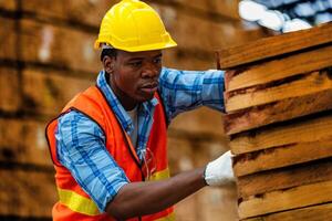 afrikanisch Arbeiter Zimmermann tragen Sicherheit Uniform und schwer Hut Arbeiten und Überprüfung das Qualität von hölzern Produkte beim Werkstatt Herstellung. Mann und Frau Arbeitskräfte Holz im dunkel Warenhaus Industrie. foto