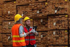 Arbeitskräfte Zimmermann tragen Sicherheit Uniform und schwer Hut Arbeiten und Überprüfung das Qualität von hölzern Produkte beim Werkstatt Herstellung. Mann und Frau Arbeitskräfte Holz im dunkel Warenhaus Industrie. foto