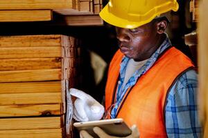 afrikanisch Arbeiter Zimmermann tragen Sicherheit Uniform und schwer Hut Arbeiten und Überprüfung das Qualität von hölzern Produkte beim Werkstatt Herstellung. Mann und Frau Arbeitskräfte Holz im dunkel Warenhaus Industrie. foto