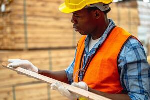 afrikanisch Arbeiter Zimmermann tragen Sicherheit Uniform und schwer Hut Arbeiten und Überprüfung das Qualität von hölzern Produkte beim Werkstatt Herstellung. Mann und Frau Arbeitskräfte Holz im dunkel Warenhaus Industrie. foto