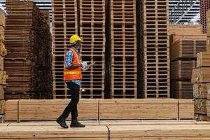 afrikanisch Arbeitskräfte Mann Ingenieurwesen Gehen und inspizieren mit Arbeiten Suite Kleid und Hand Handschuh im Bauholz Holz Lagerhaus. Konzept von Clever Industrie Arbeiter Betriebs. Holz Fabriken produzieren Holz Gaumen. foto