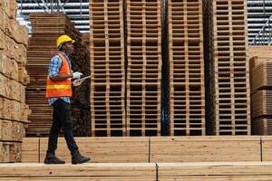 afrikanisch Arbeitskräfte Mann Ingenieurwesen Gehen und inspizieren mit Arbeiten Suite Kleid und Hand Handschuh im Bauholz Holz Lagerhaus. Konzept von Clever Industrie Arbeiter Betriebs. Holz Fabriken produzieren Holz Gaumen. foto