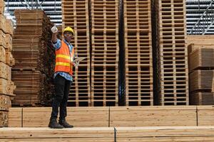 afrikanisch Arbeitskräfte Mann Ingenieurwesen Gehen und inspizieren mit Arbeiten Suite Kleid und Hand Handschuh im Bauholz Holz Lagerhaus. Konzept von Clever Industrie Arbeiter Betriebs. Holz Fabriken produzieren Holz Gaumen. foto