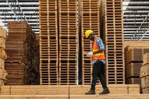 afrikanisch Arbeitskräfte Mann Ingenieurwesen Gehen und inspizieren mit Arbeiten Suite Kleid und Hand Handschuh im Bauholz Holz Lagerhaus. Konzept von Clever Industrie Arbeiter Betriebs. Holz Fabriken produzieren Holz Gaumen. foto