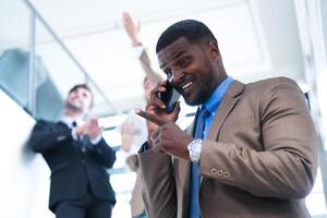 Clever schwarz Geschäftsmann Aufpassen Handy, Mobiltelefon Telefon. kahl Erwachsene Mann tragen formal tragen. nachdenklich Afroamerikaner Geschäftsmann im ein perfekt maßgeschneidert passen Stehen im Treppe im Büro. foto