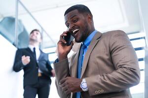 Clever schwarz Geschäftsmann Aufpassen Handy, Mobiltelefon Telefon. kahl Erwachsene Mann tragen formal tragen. nachdenklich Afroamerikaner Geschäftsmann im ein perfekt maßgeschneidert passen Stehen im Treppe im Büro. foto