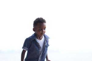 gemischt Rennen afrikanisch und asiatisch Junge ist spielen beim das draussen Bereich. lächelnd glücklich Junge hat Spaß Laufen auf das Strand. Porträt von Junge Lebensstil mit ein einzigartig Frisur. foto