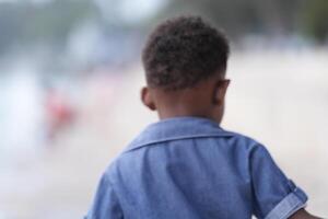 gemischt Rennen afrikanisch und asiatisch Junge ist spielen beim das draussen Bereich. lächelnd glücklich Junge hat Spaß Laufen auf das Strand. Porträt von Junge Lebensstil mit ein einzigartig Frisur. foto