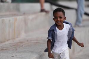 gemischt Rennen afrikanisch und asiatisch Junge ist spielen beim das draussen Bereich. lächelnd glücklich Junge hat Spaß Laufen auf das Strand. Porträt von Junge Lebensstil mit ein einzigartig Frisur. foto