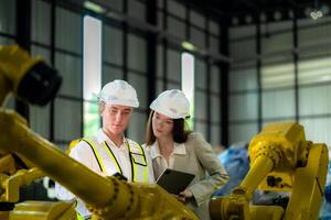 Fabrik Ingenieure inspizieren auf Maschine mit Clever Tablette. Arbeiter funktioniert beim Maschine Roboter Arm. das Schweißen Maschine mit ein Fernbedienung System im ein industriell Fabrik. künstlich Intelligenz Konzept. foto