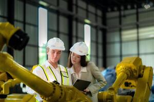 Fabrik Ingenieure inspizieren auf Maschine mit Clever Tablette. Arbeiter funktioniert beim schwer Maschine Roboter Arm. das Schweißen Maschine mit ein Fernbedienung System im ein industriell Fabrik. künstlich Intelligenz Konzept. foto