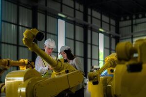 Fabrik Ingenieure inspizieren auf Maschine mit Clever Tablette. Arbeiter funktioniert beim schwer Maschine Roboter Arm. das Schweißen Maschine mit ein Fernbedienung System im ein industriell Fabrik. künstlich Intelligenz Konzept. foto