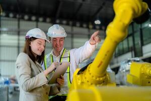 Fabrik Ingenieure inspizieren auf Maschine mit Clever Tablette. Arbeiter funktioniert beim schwer Maschine Roboter Arm. das Schweißen Maschine mit ein Fernbedienung System im ein industriell Fabrik. künstlich Intelligenz Konzept. foto