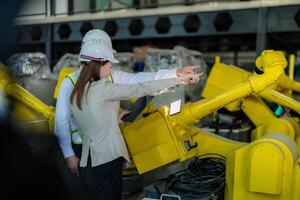 Fabrik Ingenieure inspizieren auf Maschine mit Clever Tablette. Arbeiter funktioniert beim schwer Maschine Roboter Arm. das Schweißen Maschine mit ein Fernbedienung System im ein industriell Fabrik. künstlich Intelligenz Konzept. foto