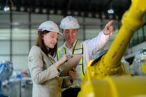 Fabrik Ingenieure inspizieren auf Maschine mit Clever Tablette. Arbeiter funktioniert beim schwer Maschine Roboter Arm. das Schweißen Maschine mit ein Fernbedienung System im ein industriell Fabrik. künstlich Intelligenz Konzept. foto