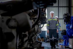 Fabrik Ingenieur Frau inspizieren auf Maschine mit Clever Tablette. Arbeiter funktioniert beim Maschine Roboter Arm. das Schweißen Maschine mit ein Fernbedienung System im ein industriell Fabrik. künstlich Intelligenz Konzept. foto