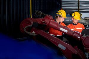 Gruppe von männlich Ingenieur Arbeitskräfte Instandhaltung automatisch Roboter Arm Maschine im ein dunkel Zimmer Fabrik. Arbeiter Überprüfung und reparieren automatisch Roboter Hand Maschine. Arbeiter tragen Sicherheit Brille und Helm. foto