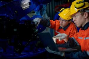 Fabrik Ingenieure inspizieren auf Maschine mit Clever Tablette. Arbeiter funktioniert beim schwer Maschine Roboter Arm. das Schweißen Maschine mit ein Fernbedienung System im ein industriell Fabrik. künstlich Intelligenz Konzept. foto