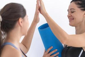 Gruppe von glücklich sportlich Frauen reden mit Körper stilvoll Sportbekleidung halten persönlich Teppiche beugte sich vor auf ein Weiß Hintergrund. warten zum Yoga Klasse oder Körper Gewicht Klasse. gesund Lebensstil und Wellness foto