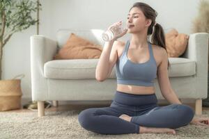 schließen oben von jung Gesicht kaukasisch Fitness Frau tragen Sport Kleider Ausbildung Innen- Trinken frisch Wasser. gesund Lebensstil und Wohlbefinden. foto