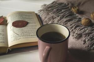 ein Tasse von Tee in der Nähe von Buch und Wolle Decke mit Dekoration durch gefallen Blätter. gemütlich Herbst. foto