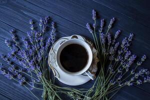 ein Tasse von Kaffee, Strauß von Lavendel und Dessert auf dunkel Blau hölzern Tisch. foto