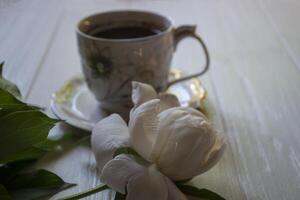 ein Tasse von Kaffee und Weiß Pfingstrose auf ein Weiß Tisch. foto