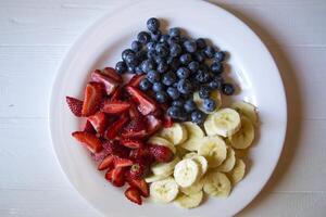 Teller mit Bananen, Erdbeeren und Blaubeeren. foto