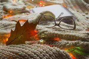 Brille, Notizblock und Herbst Blatt auf das gestrickt Plaid. Winter eben legen. Hygge Stil. foto