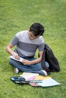 konzentriert Schüler Sitzung auf das Gras Schreiben im ein Notizbuch foto