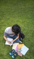 ein Schüler Sitzung auf das Gras Schreiben im ein Notizbuch foto