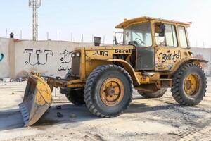 Beige Gelb Benotung Maschine geparkt im industriell Bereich von Saudi Arabien, umgeben durch Beton Menge und Weiß Wände foto