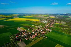 Dorf in der Nähe von Blühen Raps Felder im Landschaft, Antenne Sicht. foto