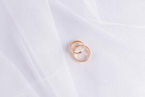 zwei Gold Hochzeit Ringe Lüge auf das Falten von ein Weiß klassisch Braut- Schleier. Hochzeit Hintergrund zum Design. Minimalismus. ein Kopieren Raum. Postkarte. Einladung. foto