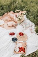 Picknick im das Wiese. Picknick Korb mit Erdbeeren, Blaubeeren, Himbeeren und Stroh Hut. foto