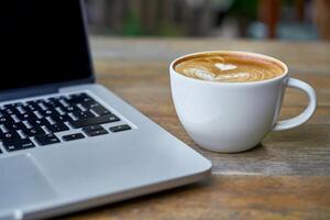 Kaffee Tasse und Laptop auf hölzern Tabelle im Kaffee Geschäft. foto